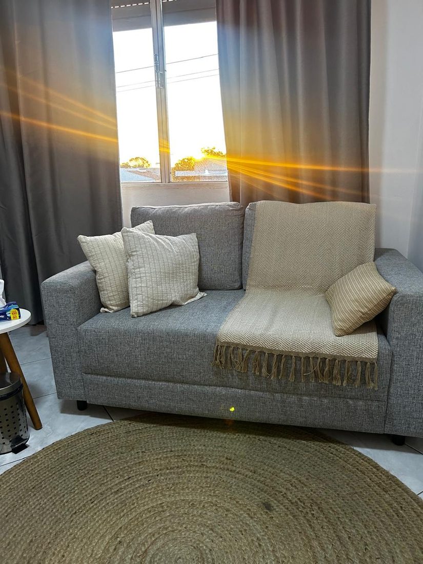 Sala de atendimento com sofá cinza, almofadas claras e sol entrando pela janela